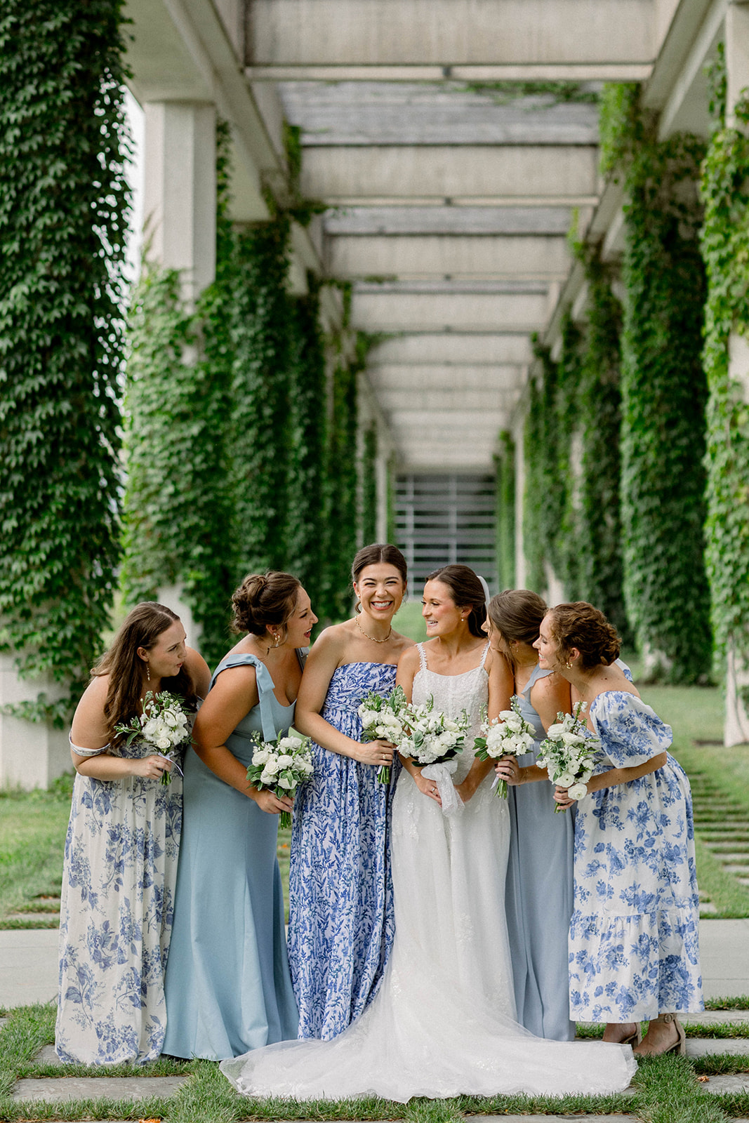 bridesmaids and bride in floral blue dresses laughing together at the Cummins Headquarters for a summer wedding in Columbus, Indiana